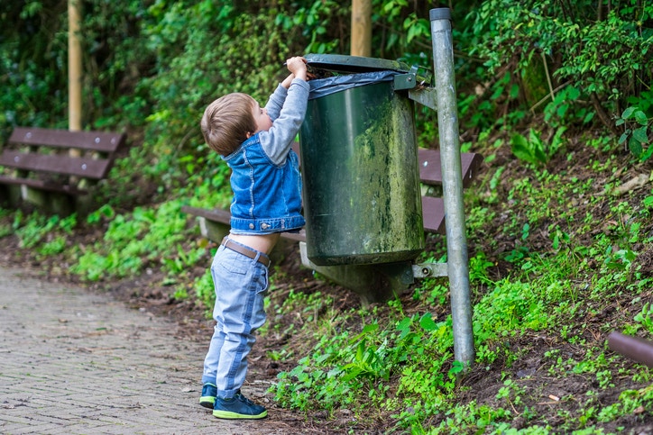 A child throwing trash in a dustbin at the street