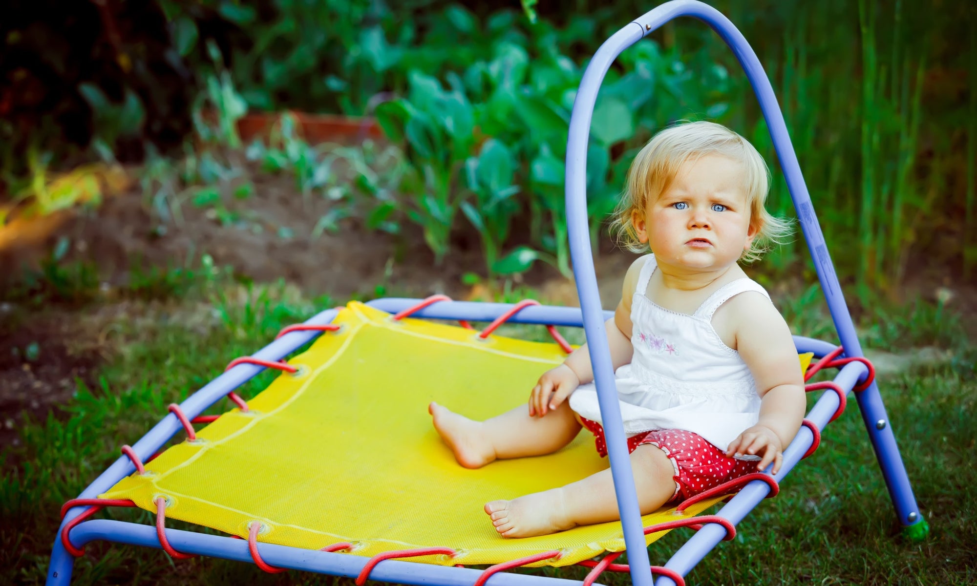 Little blonde girl sitting on a trampoline