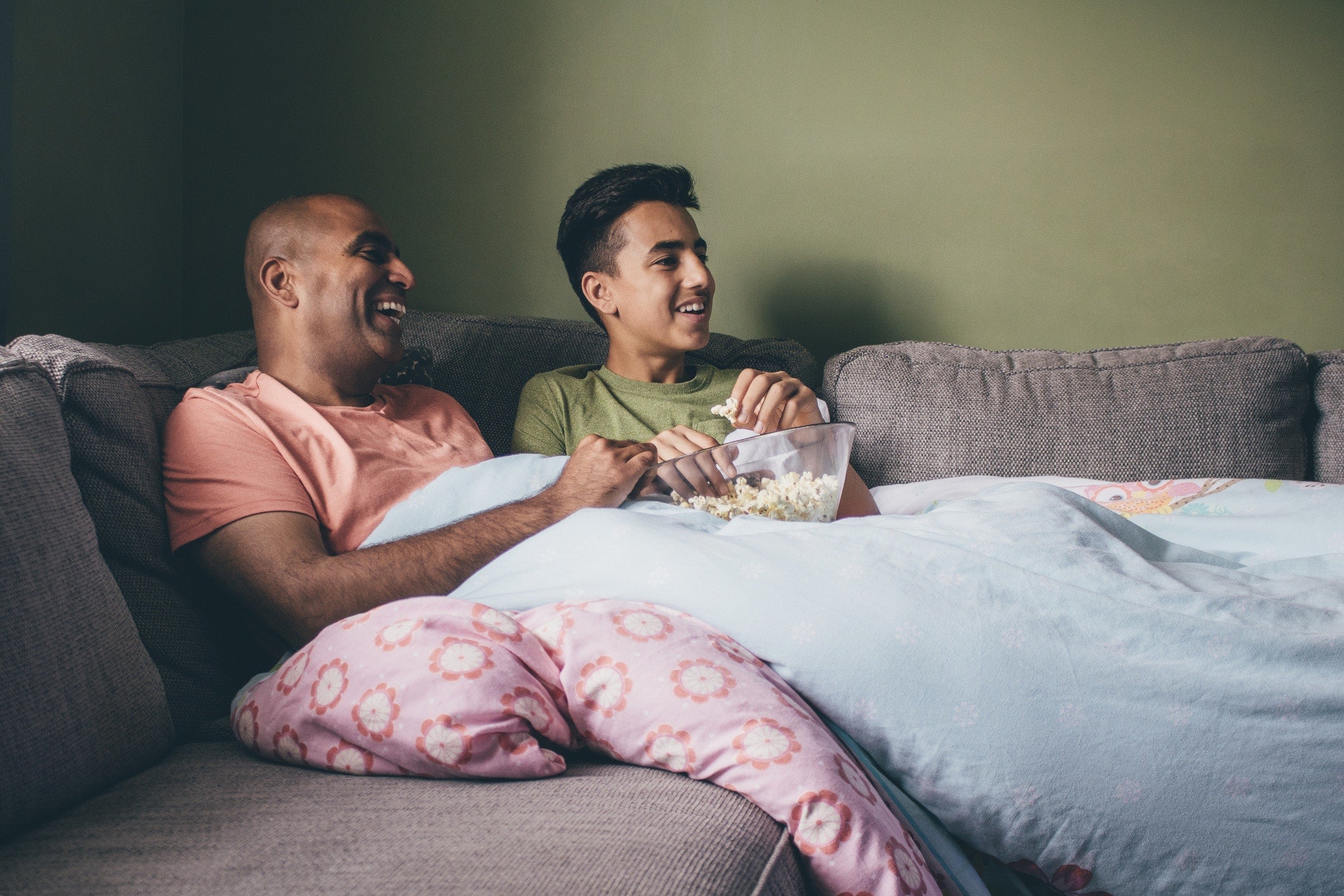 father and son watching tv and eating popcorn on sofa at home