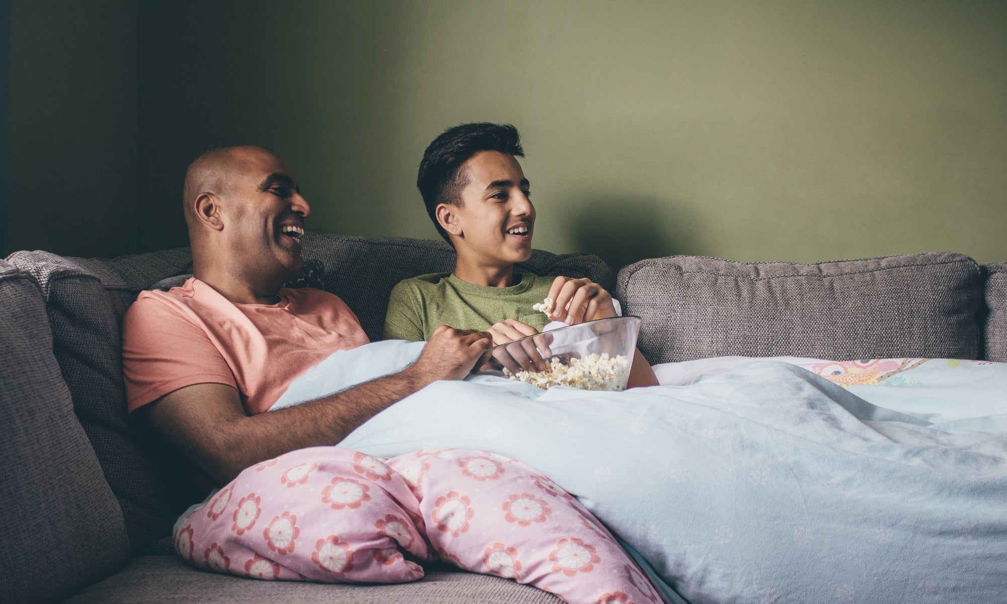 father and son watching tv and eating popcorn on sofa at home