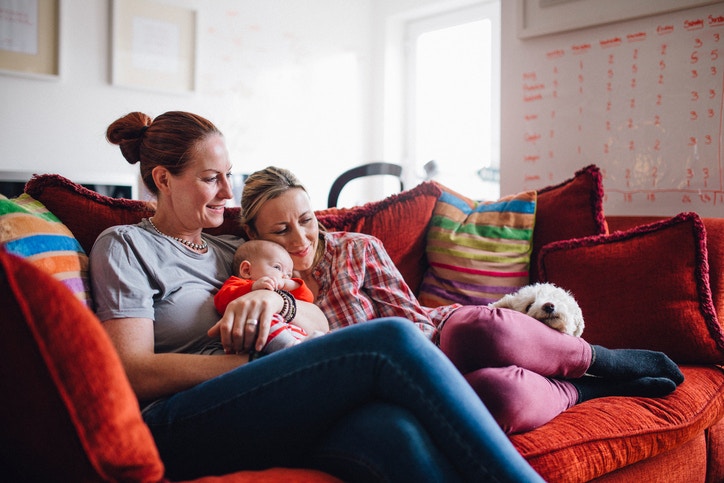 two women sitting on red couch holding new born baby