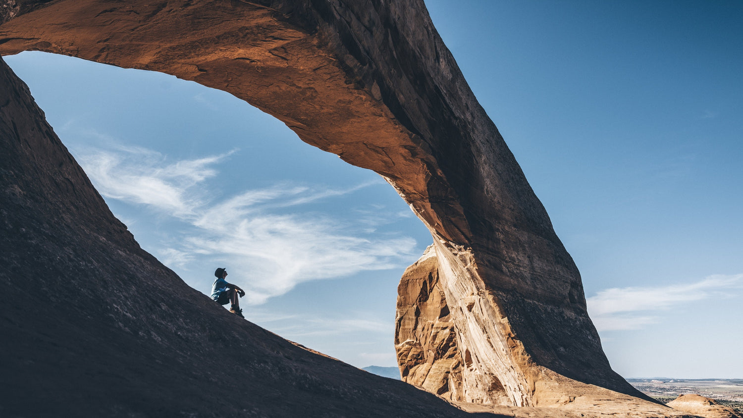 Young man sitting under arched rock