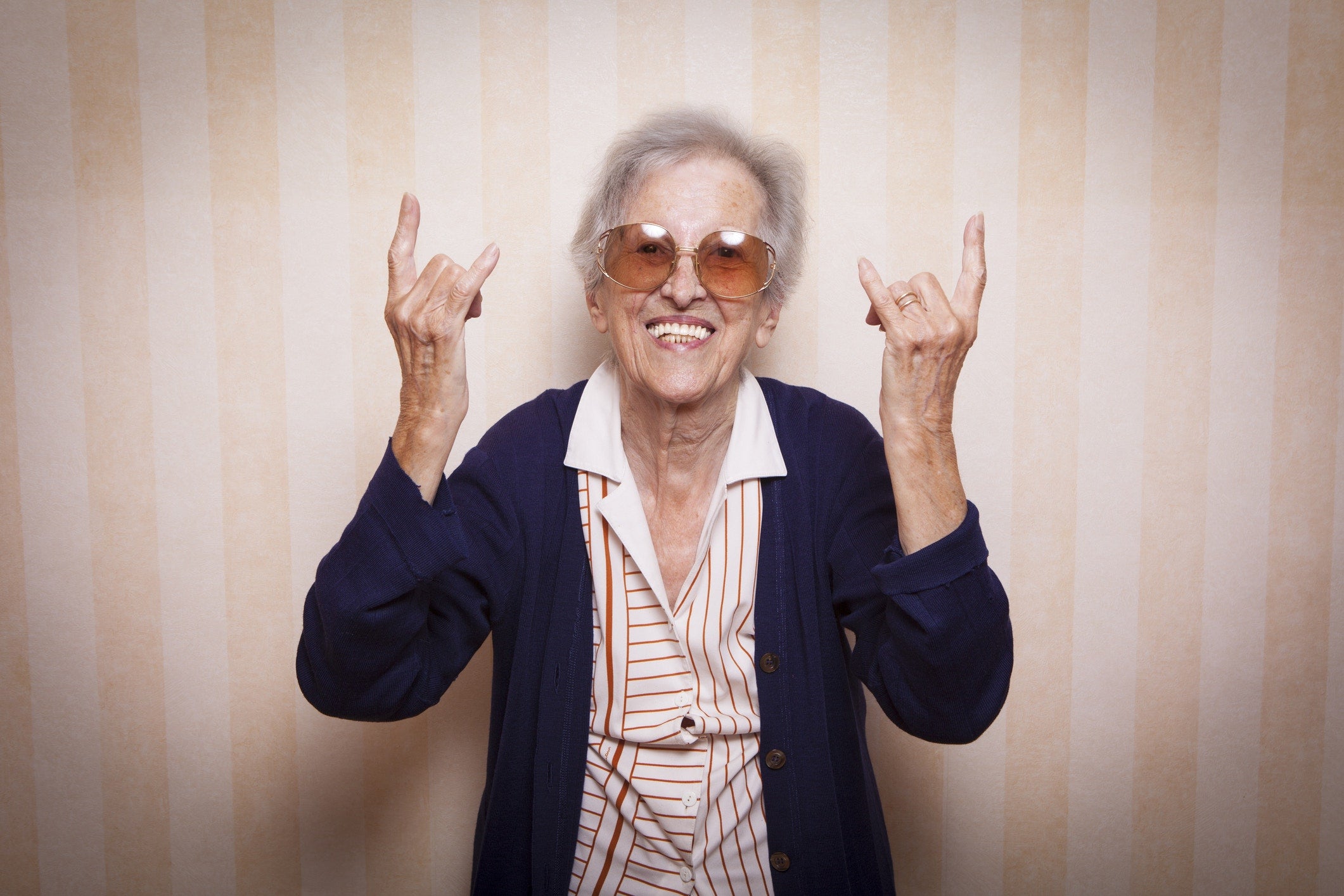 old woman wearing sunglasses and showing rock symbol