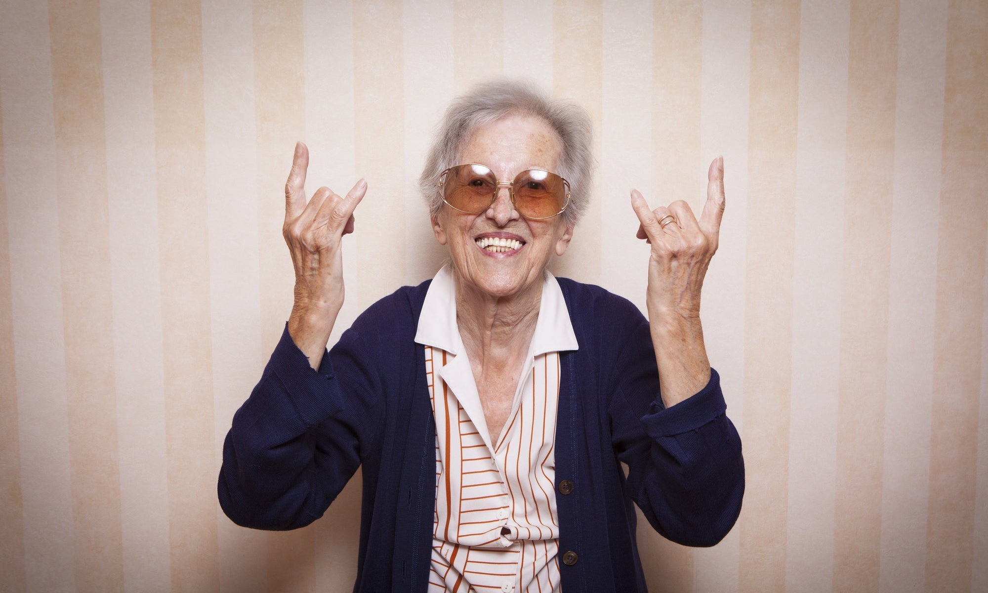 old woman wearing sunglasses and showing rock symbol