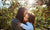 mother is kissing her daughter on the cheek, apple trees on the background