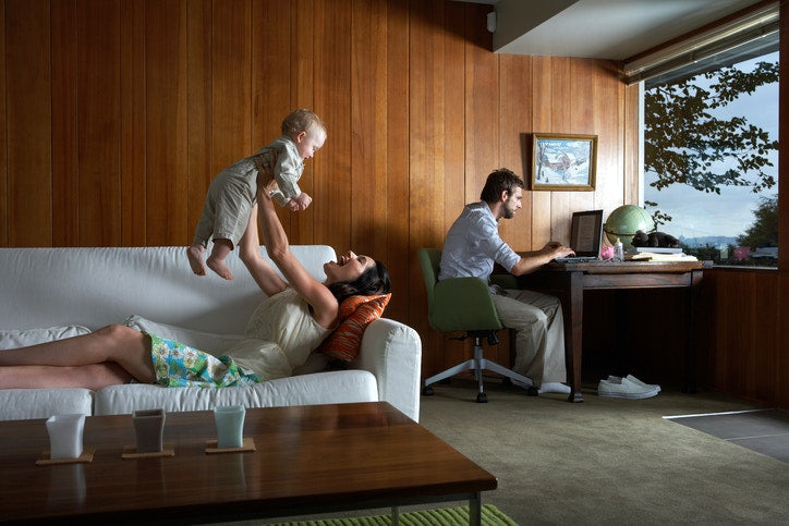 Mother playing with baby girl  while father using laptop in living room 