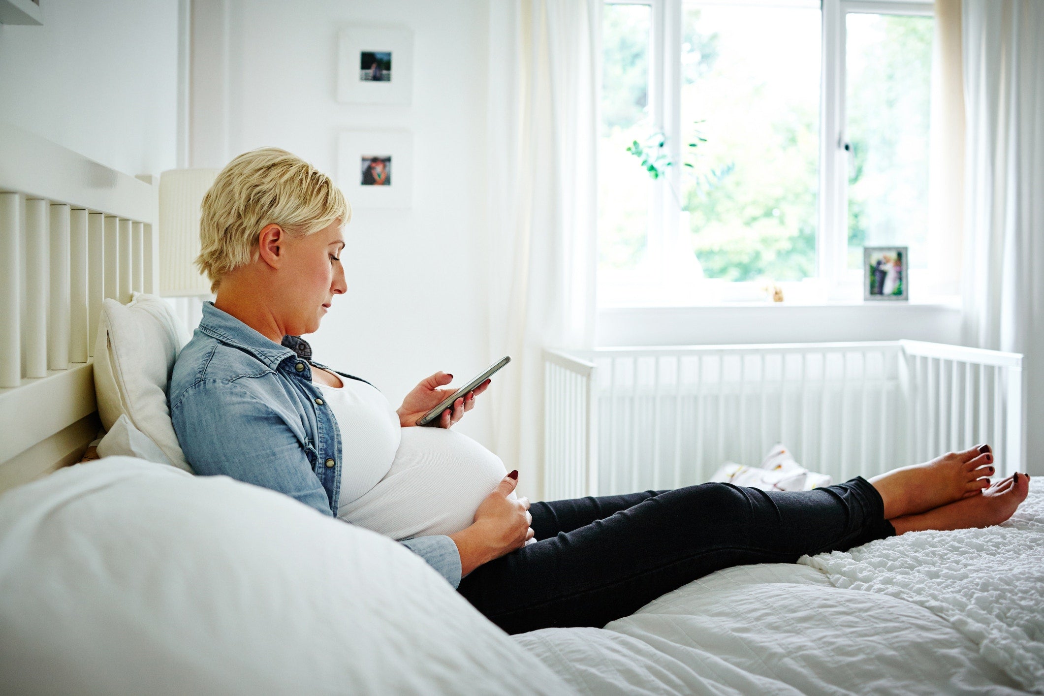 pregnant women sitting on bed and using phone