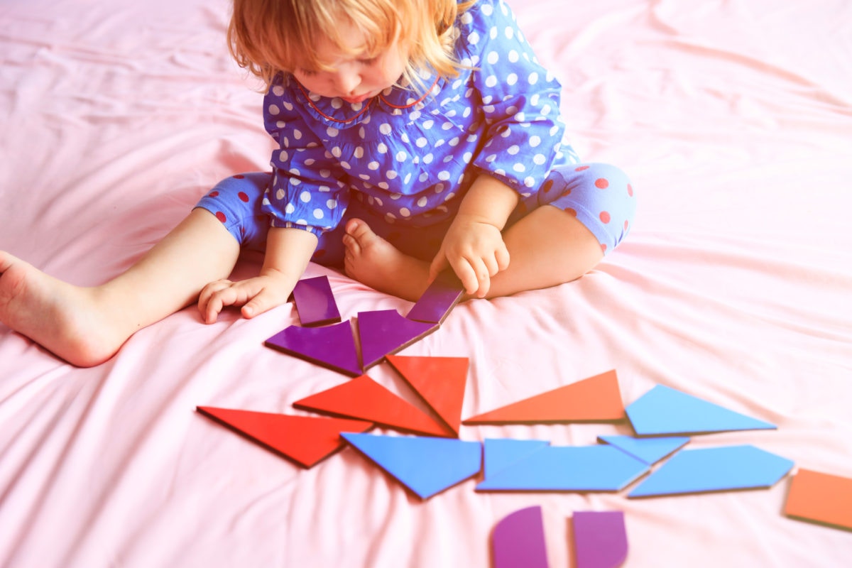 Blonde baby playing with puzzle pieces while sitting on bed