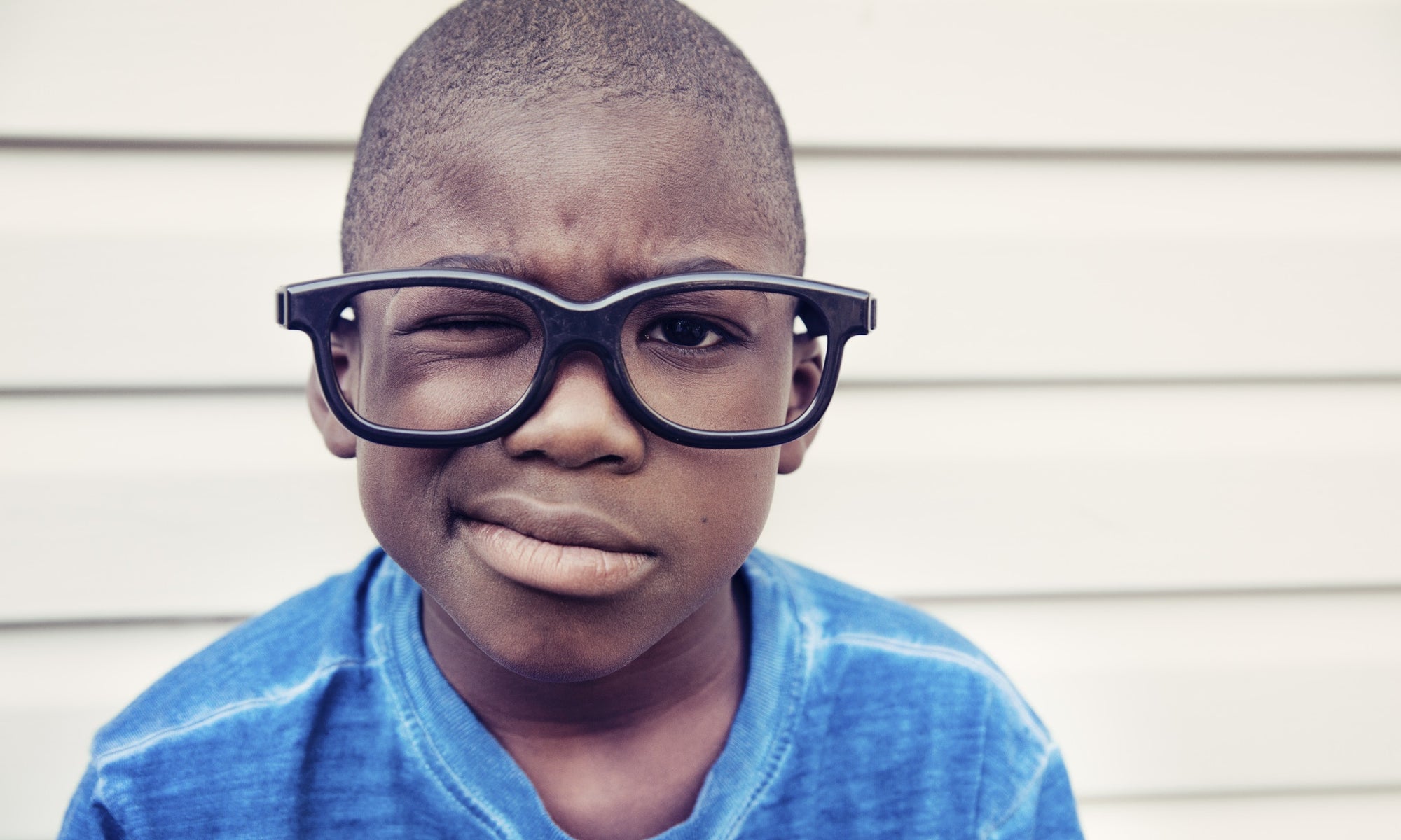 little boy with one eye closed wearing black framed glass