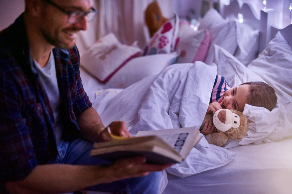 Father reading a novel in bed , child laughing and lying on bed