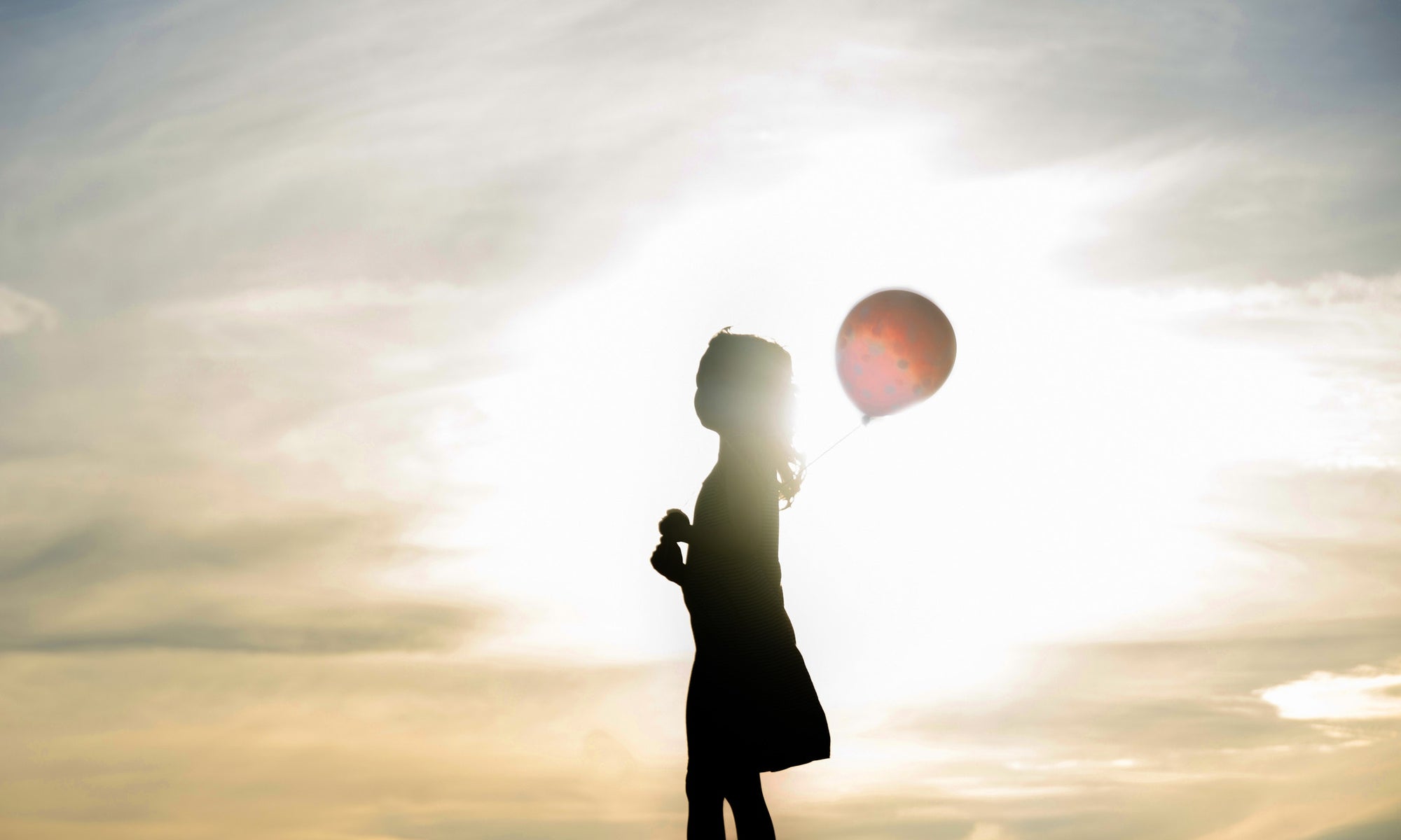 A girl is playing outside in a sunshine with ballon