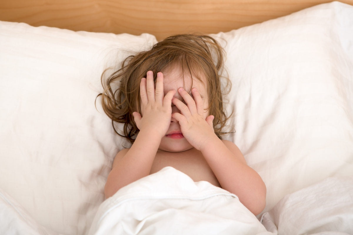 A baby is sleeping on bed by closing eyes with hands