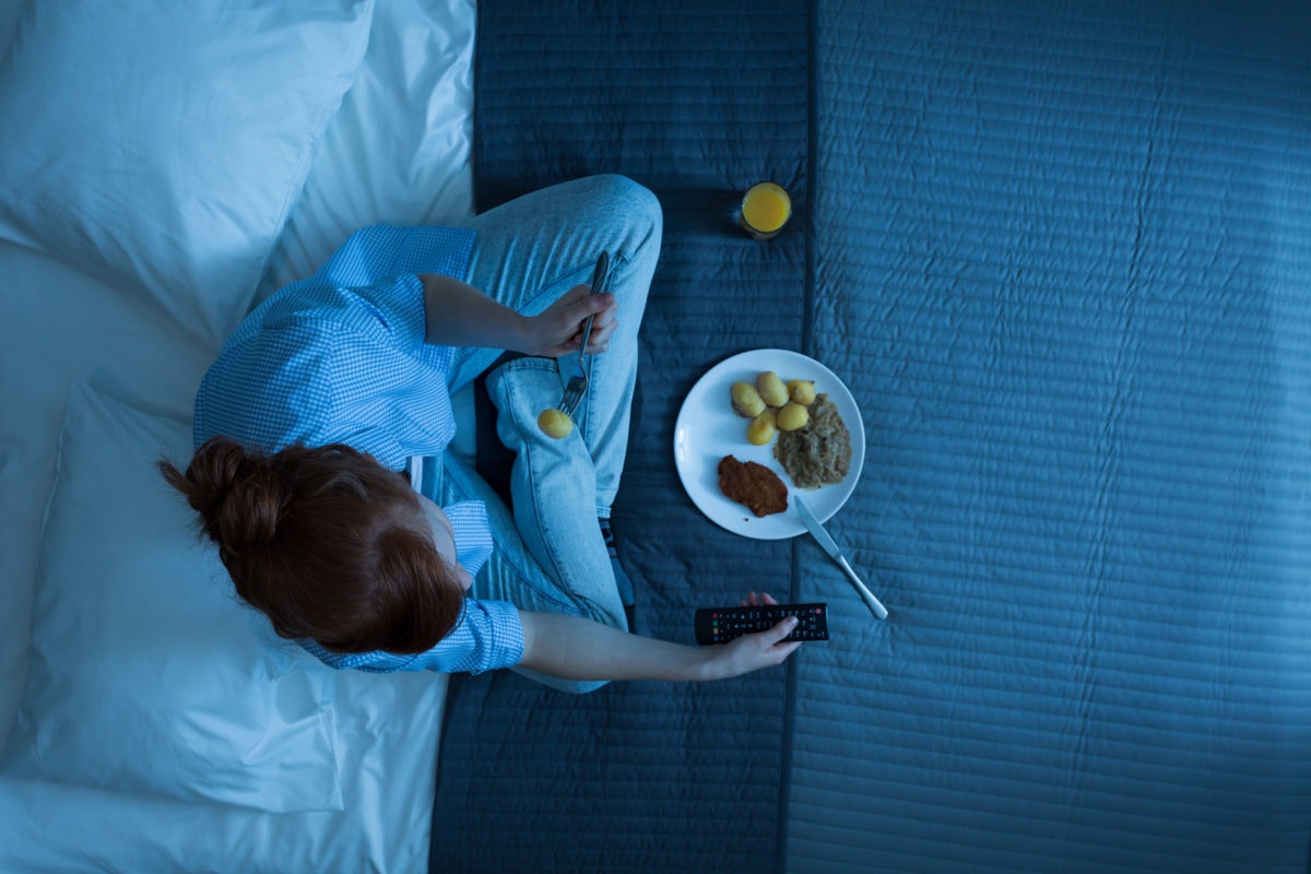 A person is having meal by holding TV remote