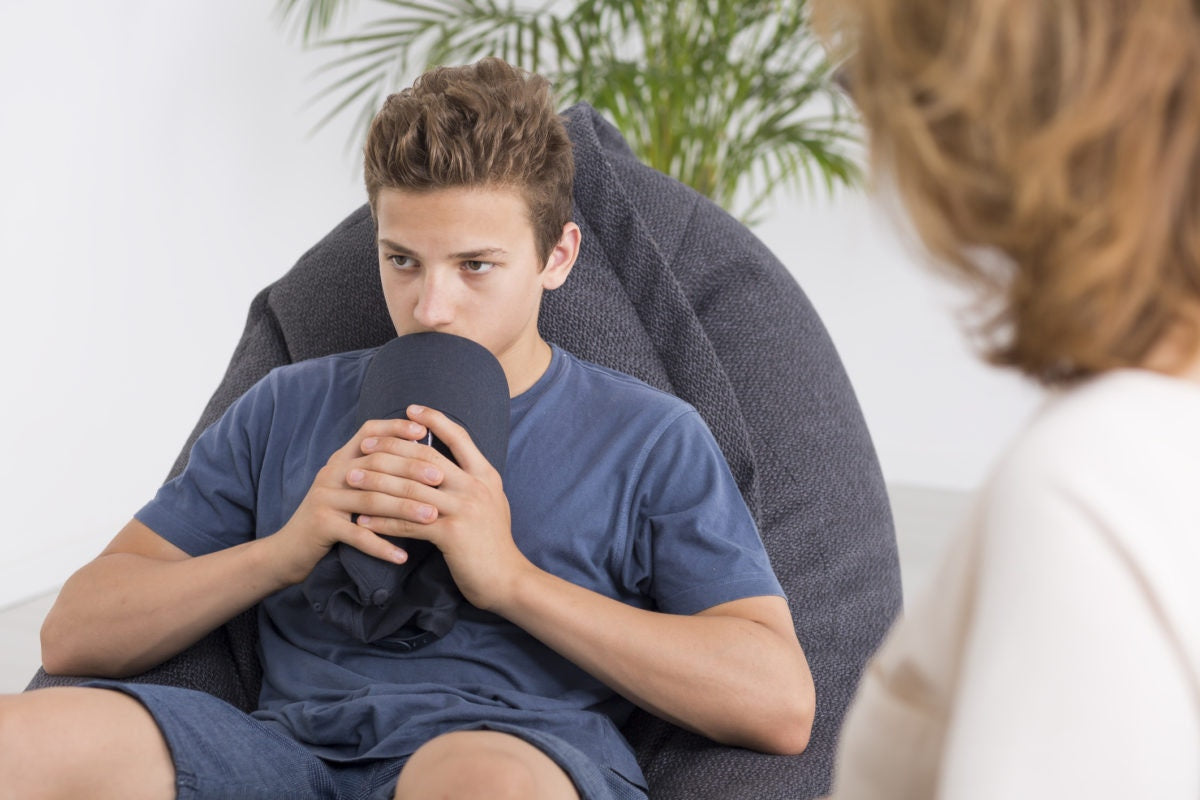 teenager boy sitting and covering his mouth using a hat