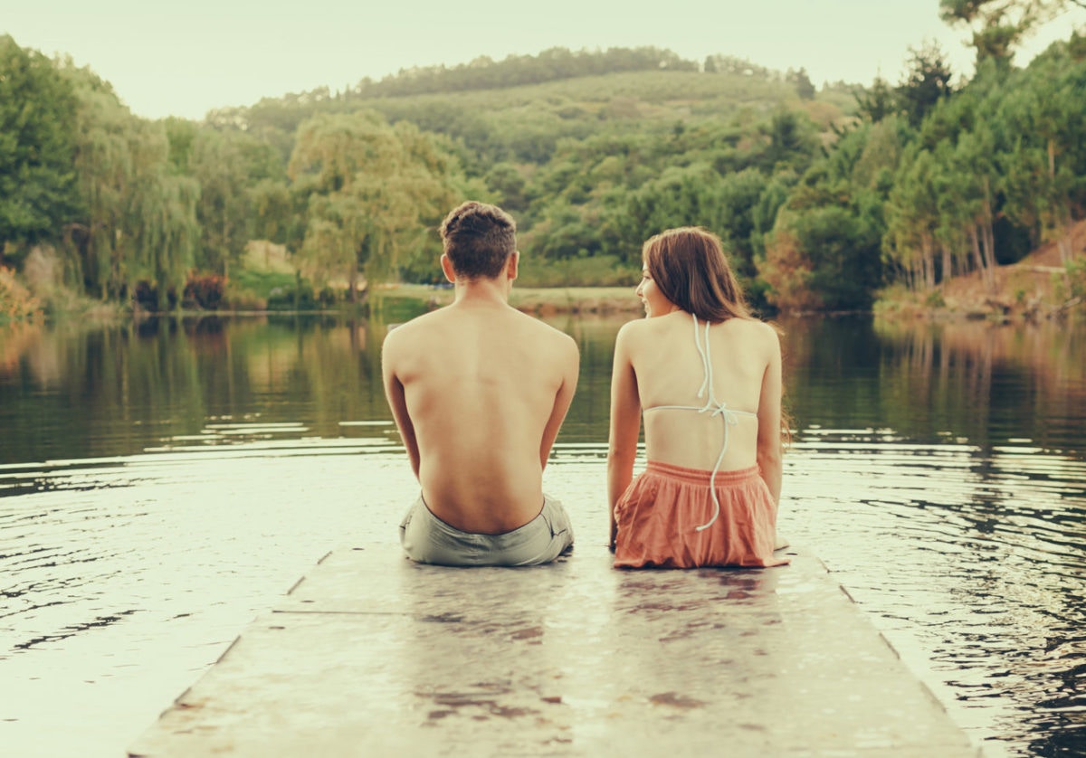 Young Couple Sitting On Dock Of A Lake