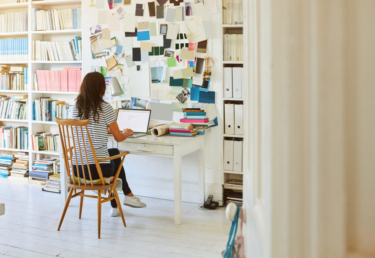 Rear view of woman sitting at the table and working on laptop in the room at home 