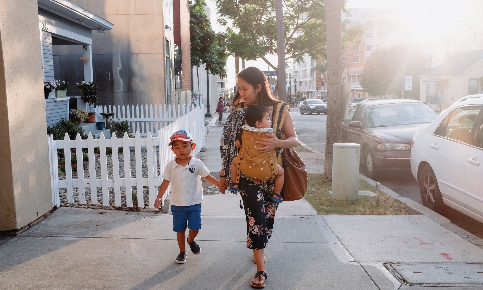 mom holing hands of one child the other in a bjorn